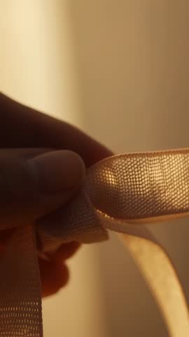 Hand tying beige ribbon bow in warm soft light vertical video