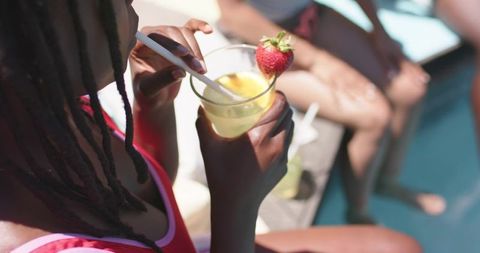 African american friends relaxing poolside sipping citrus cocktails with strawberry