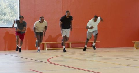 African american teammates sprinting in gym practicing defensive slides for endurance training