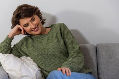 Relaxed young woman lounging on gray sofa in olive sweater for cozy lifestyle visuals