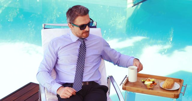 Handsome man with sunglasses drinking coffee poolside
