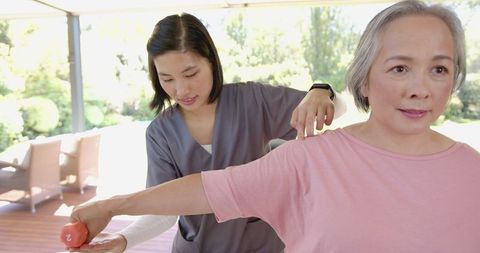 Physical therapist assisting senior woman with arm exercise using dumbbell