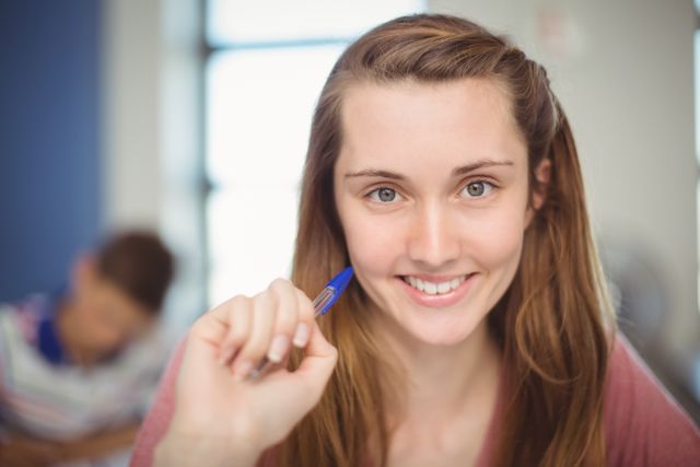 Young girl smiling while doing homework in a classroom setting. Ideal for educational content, school promotions, academic articles, and youth-focused advertisements.