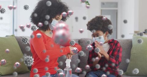 Mother and son using hand sanitizer with 3d virus graphics at home