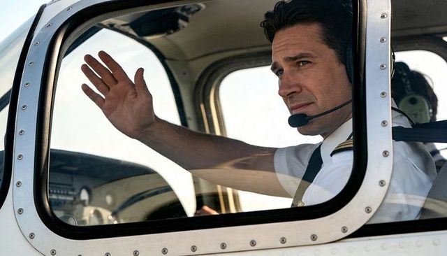 Professional pilot waving through cockpit window wearing epaulettes, tie and headset