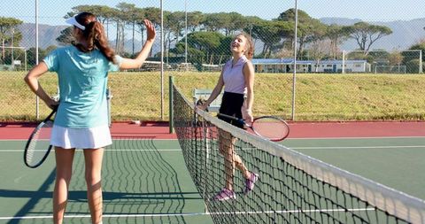 Female tennis players chatting at net on sunlit outdoor court conveying camaraderie