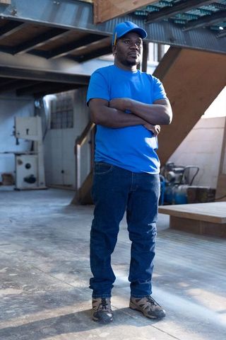 Senior african american man standing with arms crossed in workshop under metal beams