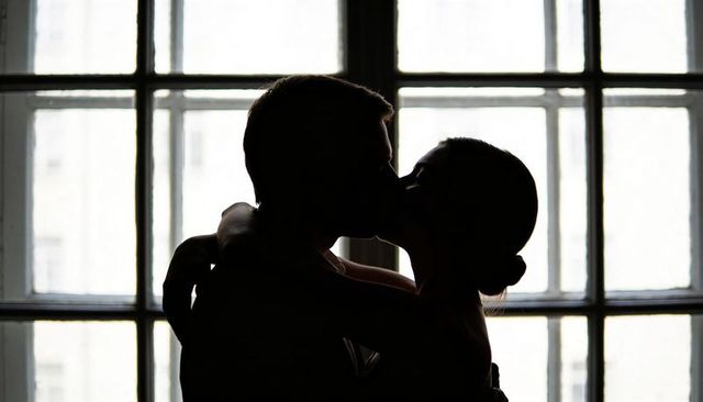 Backlit silhouette of kissing couple embracing by grid window in loft romantic interior