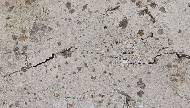 Worn concrete slab showing cracks, exposed aggregate and weathered pavement texture