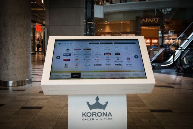 Touch screen kiosk providing store information and directions in shopping mall. Useful for showcasing modern retail technology, customer service, and navigation solutions in commercial spaces.