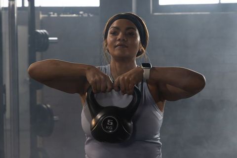 African american woman lifting 5kg kettlebell at chest wearing headband and smartwatch