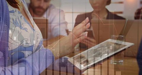 Businesswoman tapping tablet with financial charts overlay in team meeting for data analysis