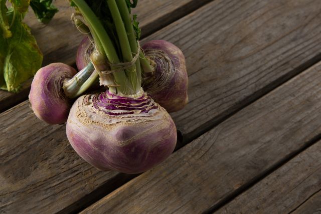 Close-up of a fresh turnip placed on a rustic wooden table. Ideal for use in articles or advertisements related to organic farming, healthy eating, gardening, and agricultural produce. Perfect for illustrating farm-to-table concepts and promoting natural, organic food.