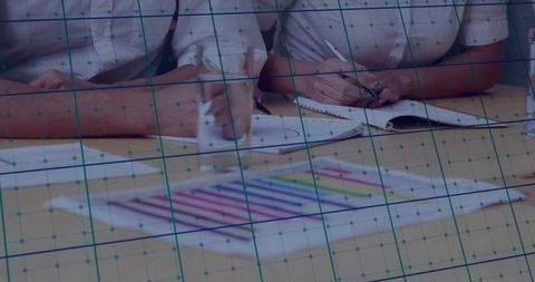 Two colleagues collaborating and taking notes over colorful charts with grid overlay