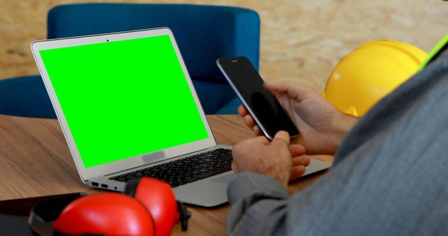 Construction worker holding smartphone next to laptop with green screen - Download Free Stock Images Pikwizard.com