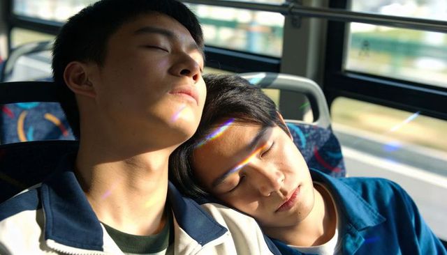 Two asian teens sleeping on bus leaning heads together during sunny transit prism light