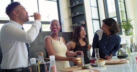 Friends laughing together on bright modern kitchen island serving flatbreads and drinks