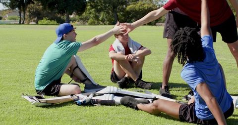 Youth cricket team high-fiving and resting on sunny park field after practice