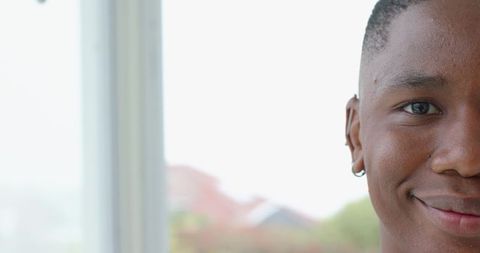 Smiling african american young man by window wearing hoop earring natural sunlight portrait