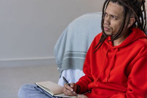 African american man journaling in red hoodie reflecting quietly in minimalist interior
