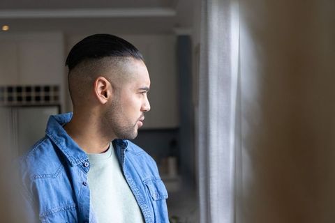 Mid adult man gazing through curtained window in sunlit modern kitchen, contemplative domestic portr