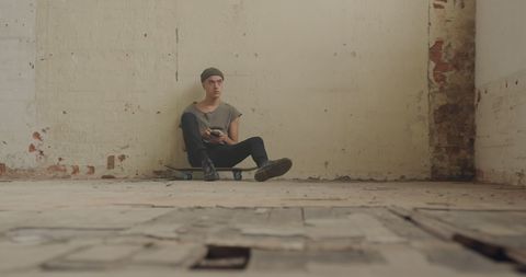 Contemplative Young Man Sitting on Skateboard Indoors with Rustic Background - Download Free Stock Images Pikwizard.com