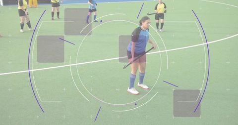 Female field hockey player standing on green turf holding stick with purple hud overlays
