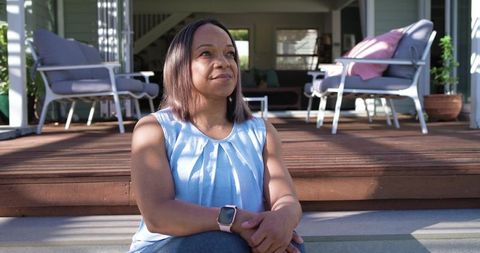Mature african american woman sitting on porch steps wearing smartwatch, reflecting sunlight