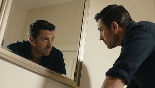 Man leaning over mirror contemplating reflection in quiet interior moment of introspection