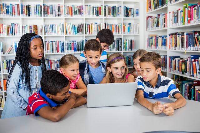 Children gathered around a laptop in a library, engaging in collaborative learning. Ideal for educational content, school promotions, technology in education, and teamwork concepts.