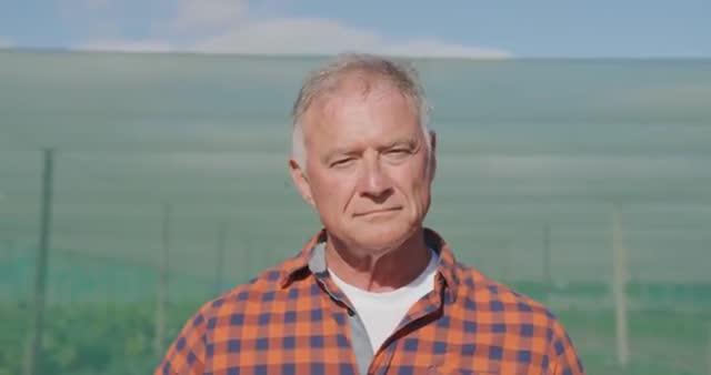 Middle-aged male farmer standing in an organic agricultural setting with a focused expression. Ideal for illustrating articles or media related to organic farming, sustainable agriculture, and rural lifestyle. Useful for agricultural magazines or sustainable lifestyle blogs showcasing traditional farming practices.