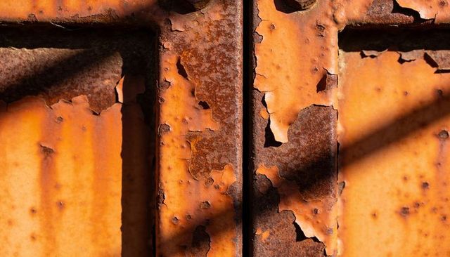 Peeling orange paint revealing rusted metal texture on weathered container panel