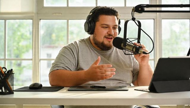 Friendly podcaster recording live show with boom microphone and laptop in bright home studio