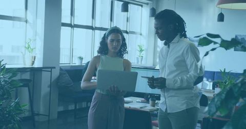 Two colleagues reviewing laptop in modern open office with plants and daylight while collaborating