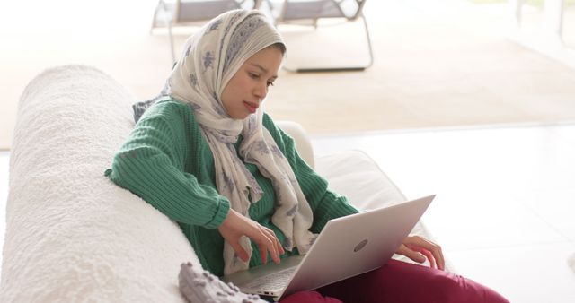 Woman in Hijab Using Laptop on Couch in Bright Living Room - Download Free Stock Images Pikwizard.com