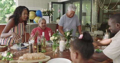 Multigenerational family celebrating at sunroom table, serving bread and sharing laughter