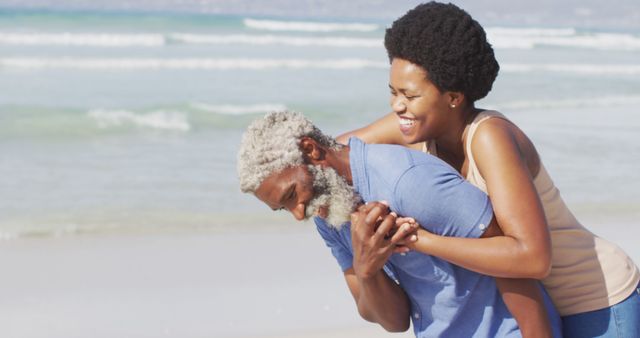 Happy african american couple walking and embracing on sunny beach. healthy and active time beach holiday.