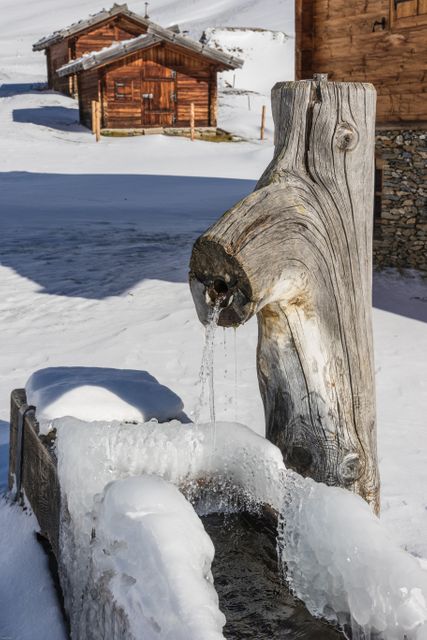 Traditional wooden fountain located in a serene, snowy mountain setting, ideal for capturing winter outdoor scenes, showcasing traditional Alpine architecture, or illustrating concepts related to nature, cold weather, and rustic living.