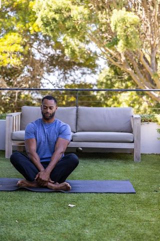 African american man practicing yoga and meditation on sunny patio for relaxation