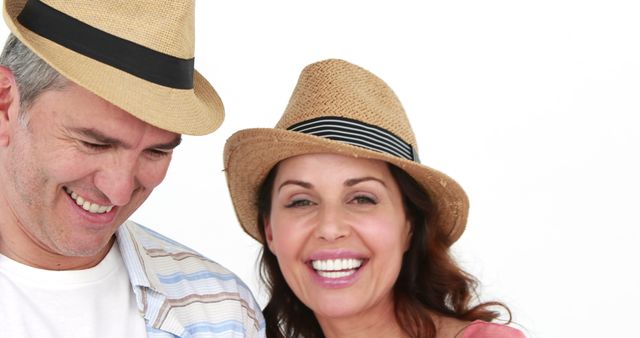 Middle-aged couple wearing straw hats and casual summer clothes, smiling and enjoying a moment together against a plain white background. Great for content related to summer lifestyle, mature relationships, happiness, and casual fashion. Can be used in advertisements, social media, blog posts or articles on middle-aged love and joy.