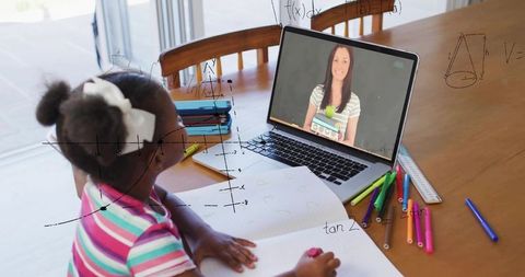 Young girl learning math online at table with laptop and workbook for remote tutoring