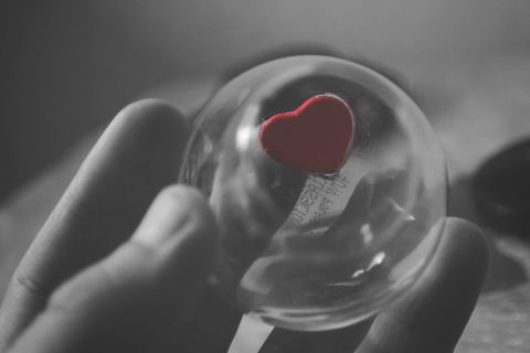 Hand holding glass sphere with red heart symbol