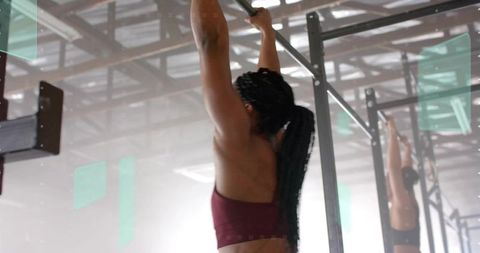 Mid adult woman pulling on pull-up bar wearing maroon sports bra at crossfit rig
