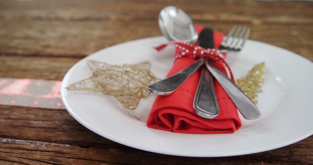 A festive table setting features a red napkin tied with a ribbon around silverware, accompanied by a decorative star, with copy space. It evokes a holiday atmosphere, set for a Christmas meal.