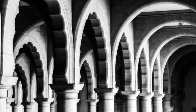 Scalloped stone arches colonnade in historic cloister dramatic light shadow minimalist