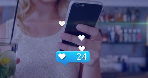 Woman holding smartphone and sipping cocktail while receiving social media likes