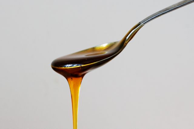 Golden honey spilling from spoon, against plain white background, indicating sweetness and natural food product. Great for illustrating healthy eating, food blogs, recipes involving honey, advertisements for honey products, and natural remedy promotions.