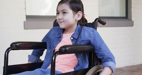 Asian girl sitting in manual wheelchair wearing denim jacket smiling outdoors