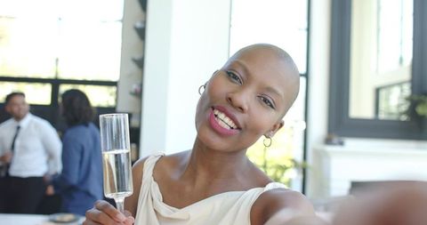 Smiling african american woman holding champagne flute taking selfie at celebration