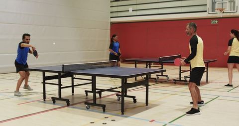 Friends Playing Competitive Doubles Table Tennis in Gymnasium